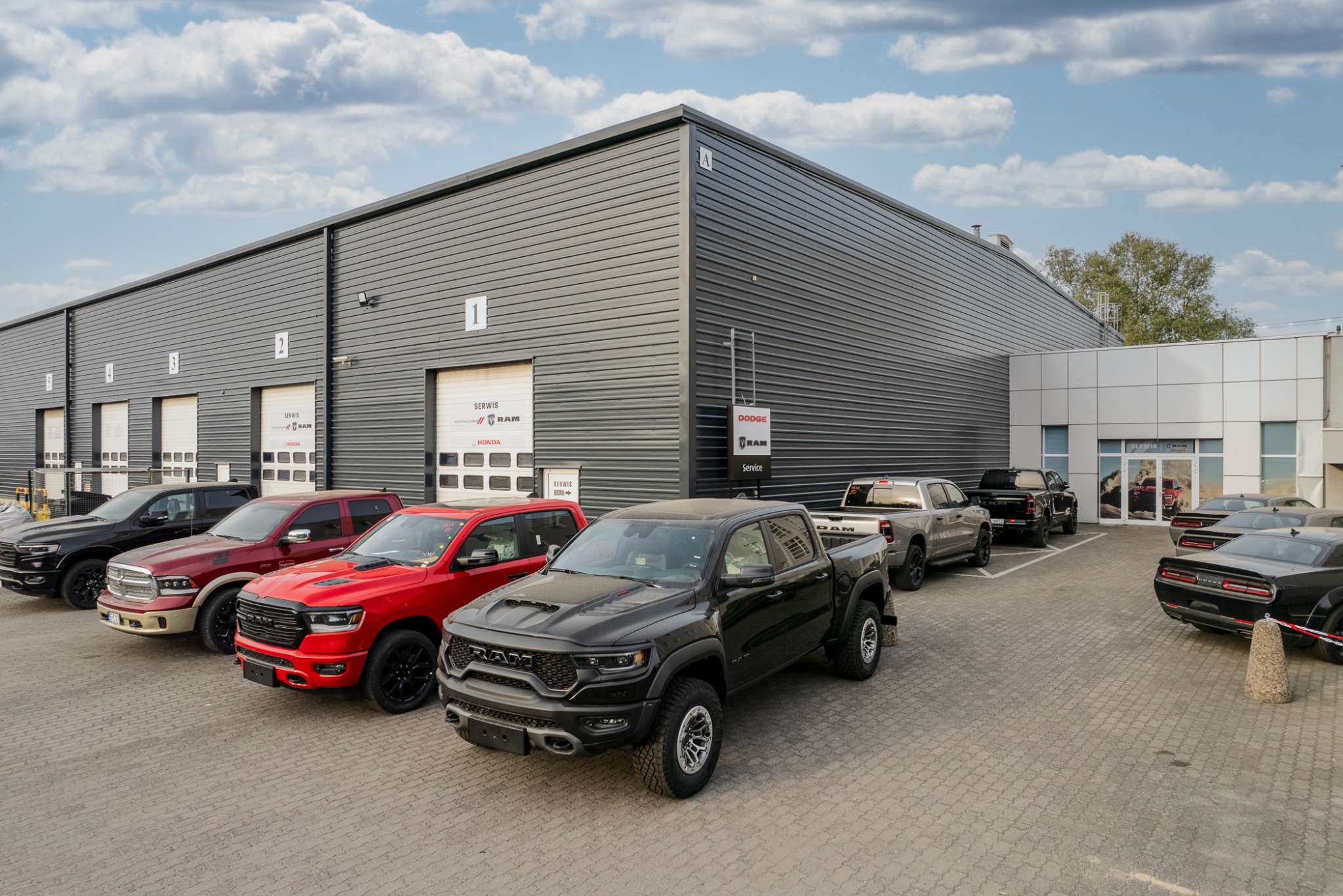 Rząd zaparkowanych samochodów marki RAM przed budynkiem serwisu z logo RAM i Dodge nad bramami garażowymi.
