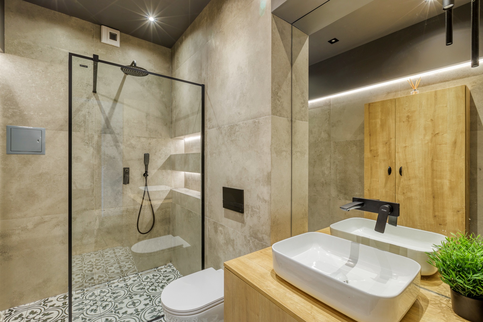 Nowoczesna łazienka z kabiną prysznicową typu walk-in, umywalką nablatową i szafką z drewnianym fornirem, wykończona w beżowych odcieniach z akcentami czerni.