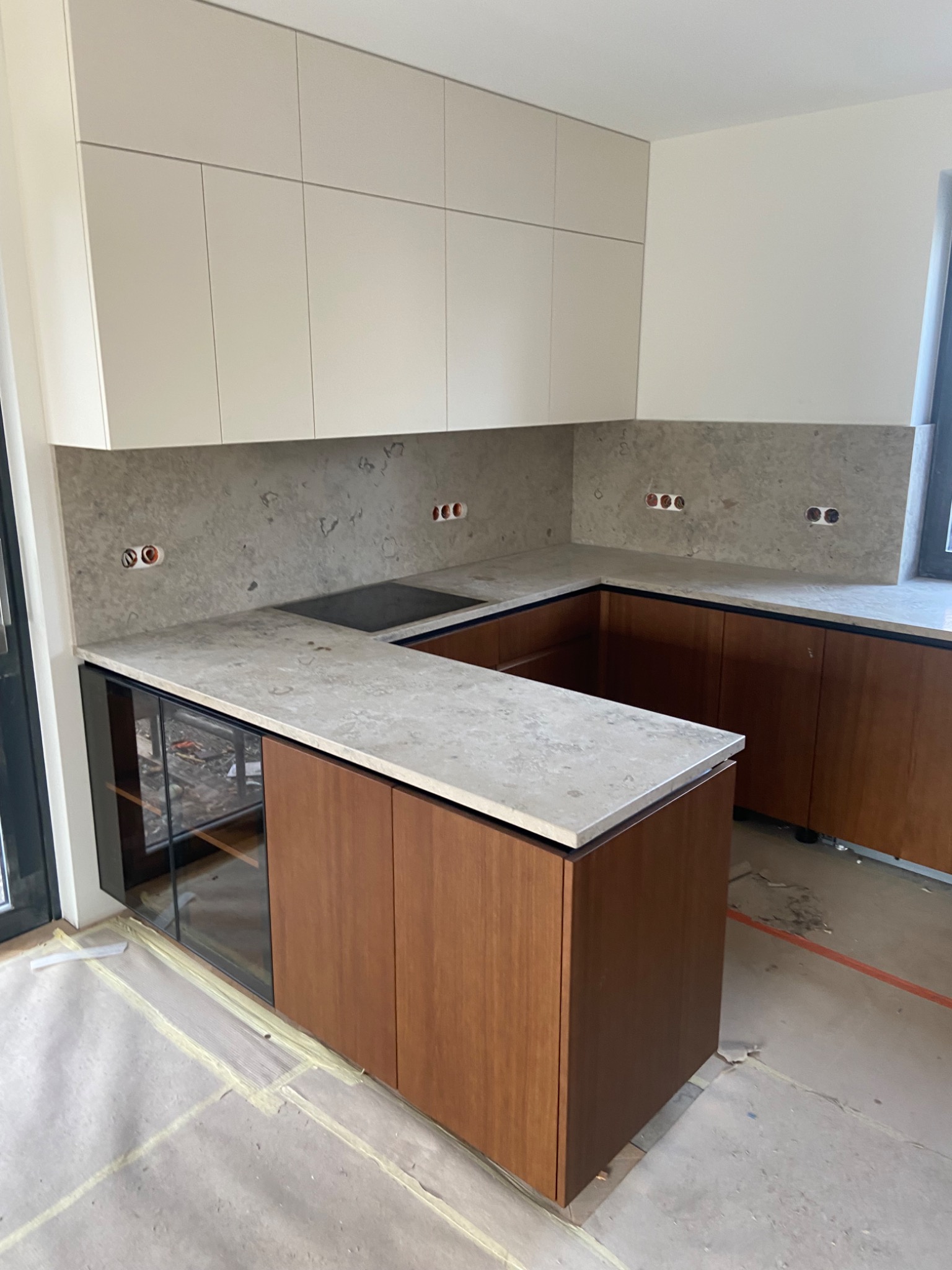 Nowoczesna kuchnia w trakcie wykańczania, z szarym blatem i brązowymi szafkami, widoczne gniazdka elektryczne i zabezpieczona podłoga.
