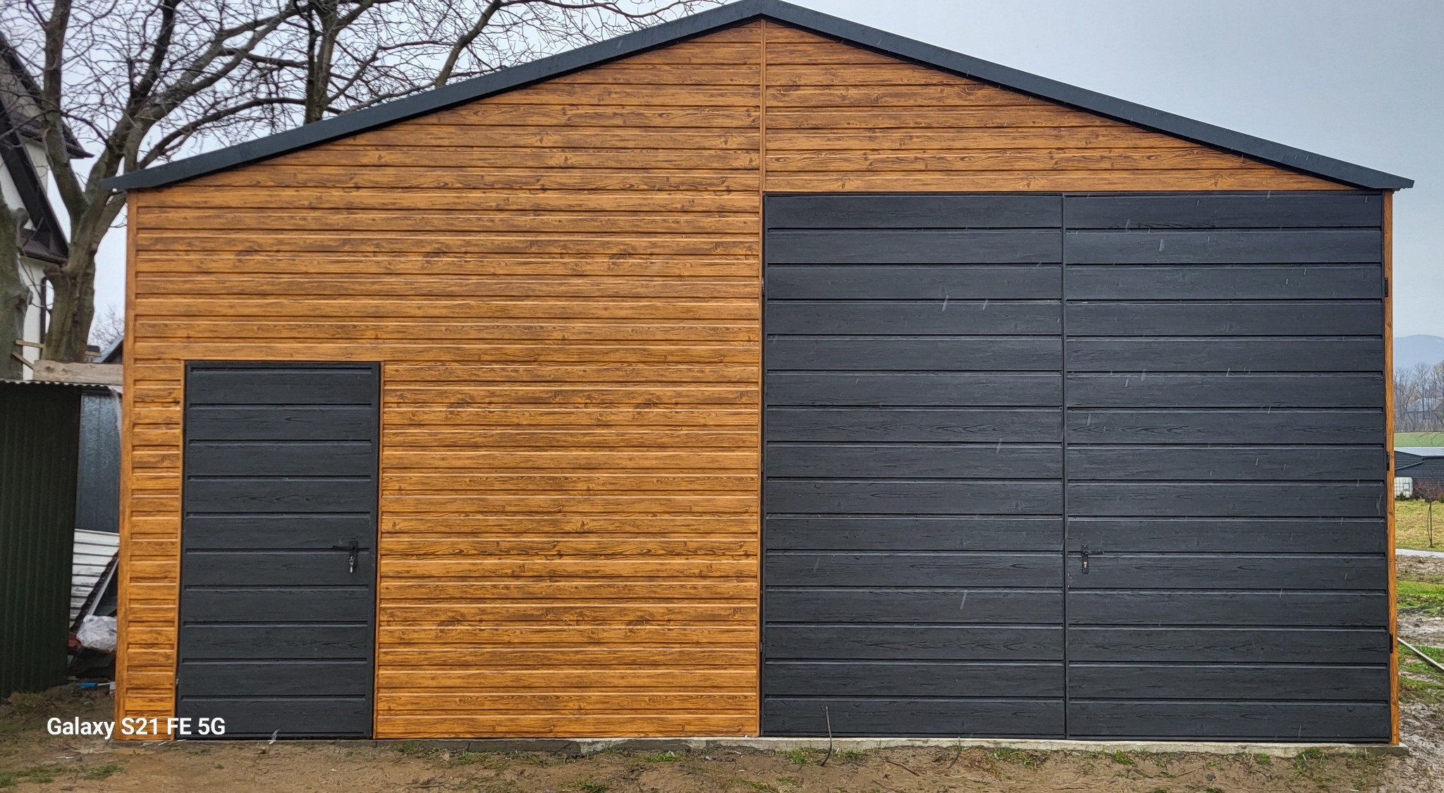 Gotowy garaż z blachy drewnopodobnej z dwiema bramami: jedna duża, dwuskrzydłowa, druga mniejsza, pojedyncza, obie w kolorze grafitowym.