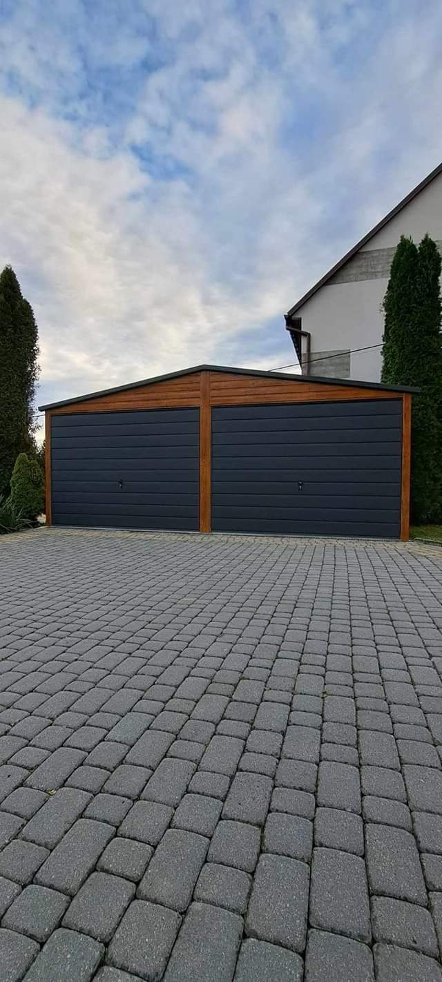 Dwustanowiskowy garaż blaszany z drewnopodobną ramą i antracytowymi bramami segmentowymi, ułożony na kostce brukowej.