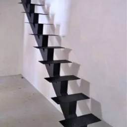 Czarne, metalowe schody wspornikowe, przymocowane do ściany, w surowym wnętrzu, widoczne elementy konstrukcyjne stropu.