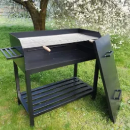 Czarny, metalowy grill ogrodowy z rusztem i dolną półką, na tle kwitnącego drzewa w słoneczny dzień.