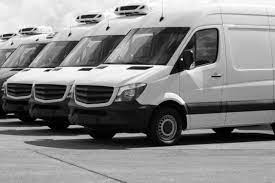 Szereg białych samochodów dostawczych z zabudową chłodniczą, ustawionych jeden za drugim na placu, widok z boku, lekko z dołu.