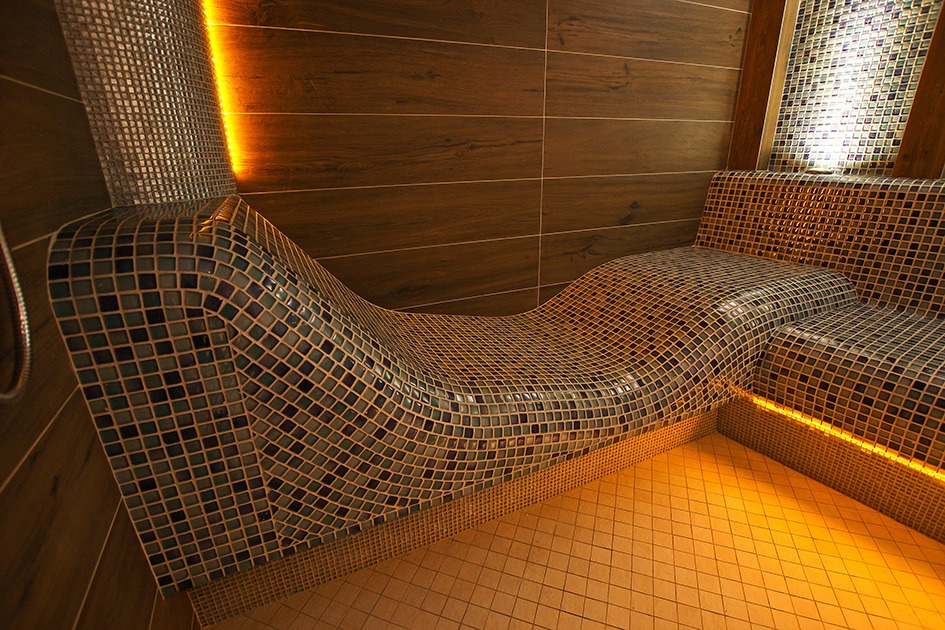 Wnętrze relaksacyjne z mozaikową, profilowaną leżanką i drewnianymi panelami ściennymi, oświetlone ciepłym, punktowym światłem.