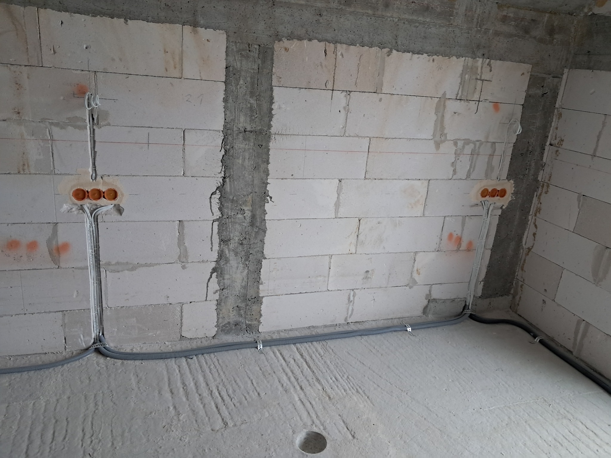 Surowy stan: ściany z betonu komórkowego z wyciętymi otworami pod gniazdka elektryczne i poprowadzonymi przewodami w szarych rurkach, przymocowanymi metalowymi uchwytami.