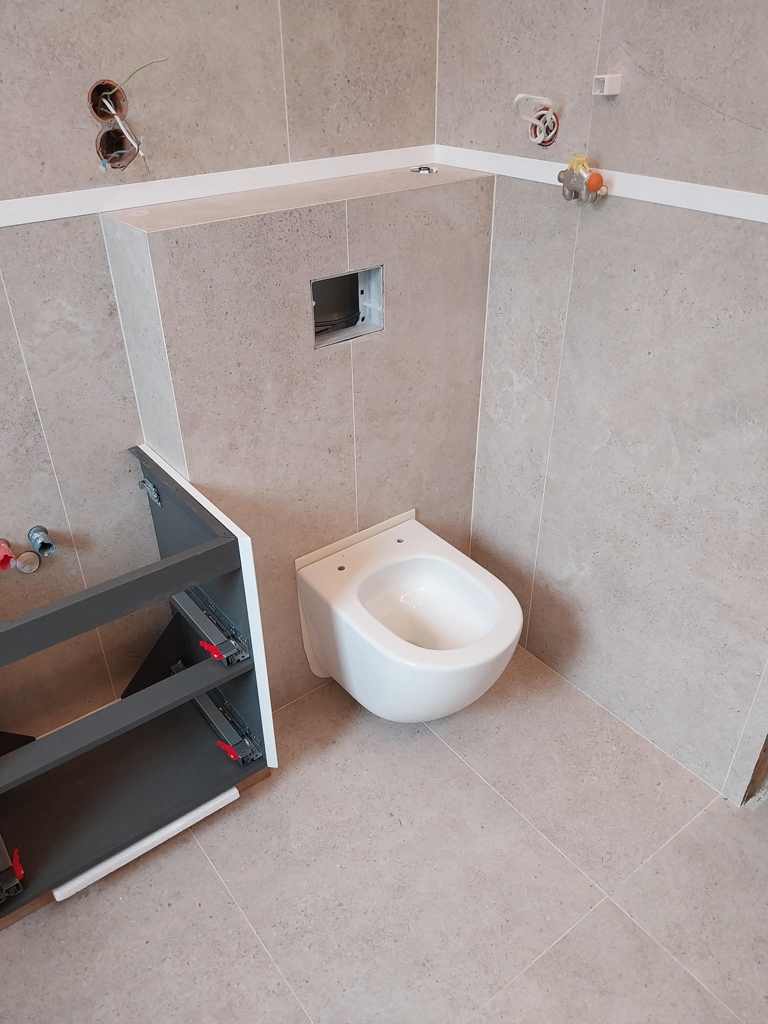 Montaż podwieszanej toalety i szafki pod umywalkę w łazience w Białymstoku, widoczne instalacje elektryczne i hydrauliczne.