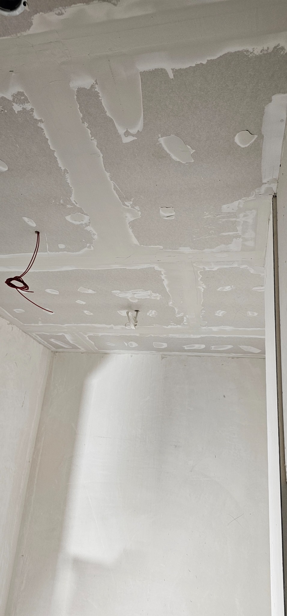Surowy sufit z płyt kartonowo-gipsowych, częściowo pokryty szpachlą, widoczne kable elektryczne i fragment ściany, przygotowanie do dalszych prac wykończeniowych.