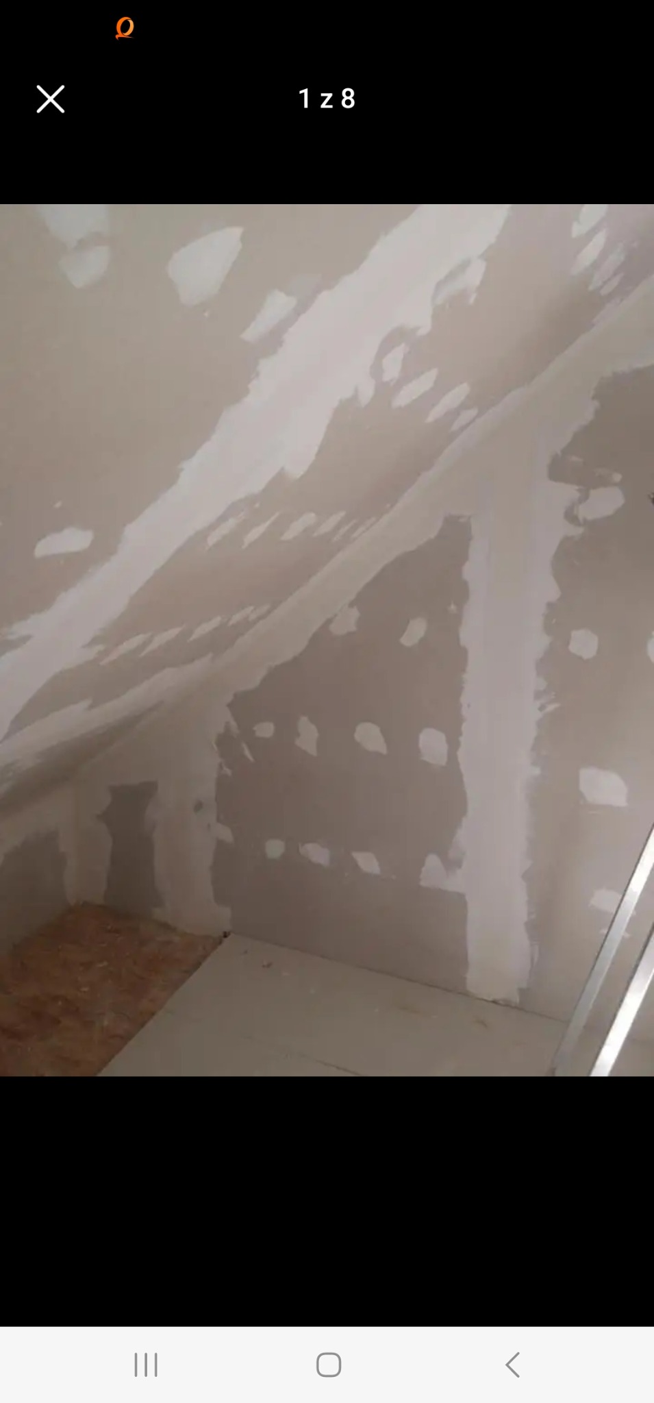 Poddasze w trakcie prac wykończeniowych, ściany pokryte gładzią szpachlową, widoczne nierówności i białe plamy, fragment podłogi wyłożony płytą OSB, drabina oparta o ścianę.