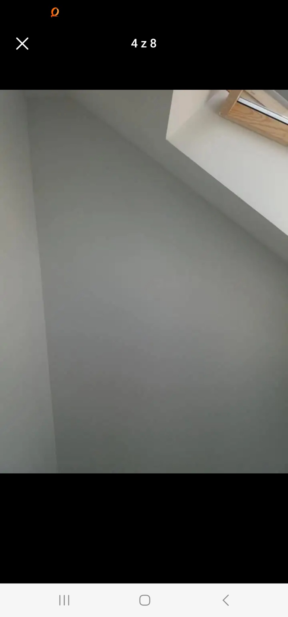 Świeżo pomalowana szara ściana pod skosem, widok na okno dachowe z drewnianą ramą.