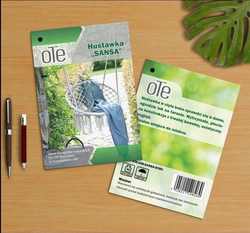 Dwie ulotki reklamowe huśtawki ogrodowej 'SANSA' marki Ole na drewnianym blacie, obok leżą dwa długopisy, w tle liść monstery.
