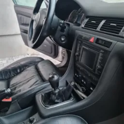 Wnętrze samochodu Audi A6 C5 z czarną skórzaną tapicerką, widoczny kokpit, kierownica z logo, lewarek zmiany biegów i panel sterowania z nawigacją.