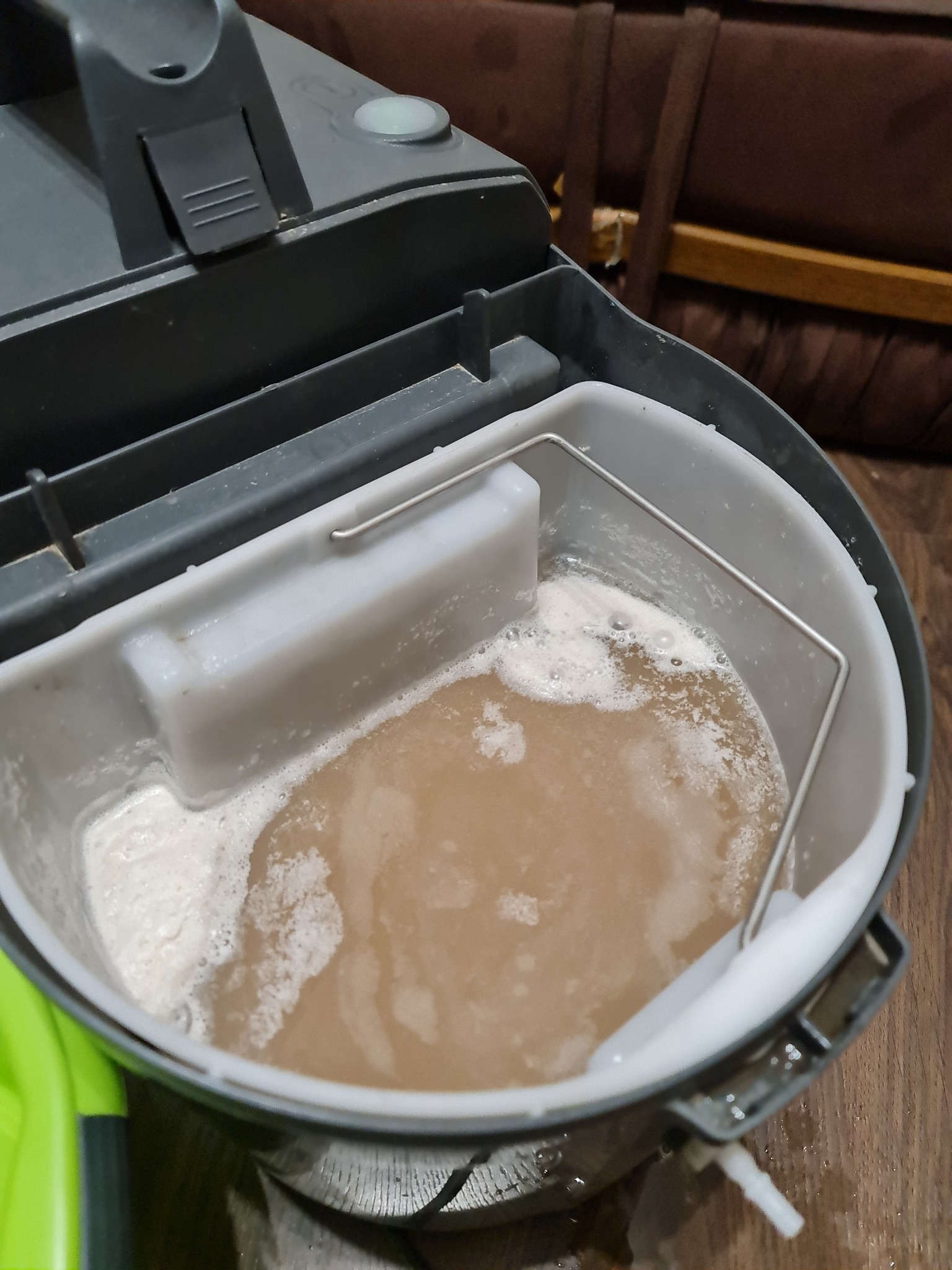 Zbiornik na brudną wodę w odkurzaczu piorącym, wypełniony brudną, spienioną cieczą po zakończonym procesie czyszczenia, widoczne osady na dnie.