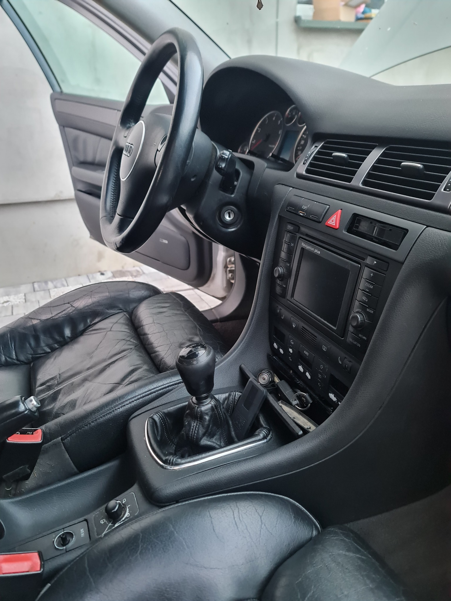 Wnętrze samochodu Audi A6 C5 z czarną skórzaną tapicerką, widoczny kokpit, kierownica z logo, lewarek zmiany biegów i panel sterowania z nawigacją.