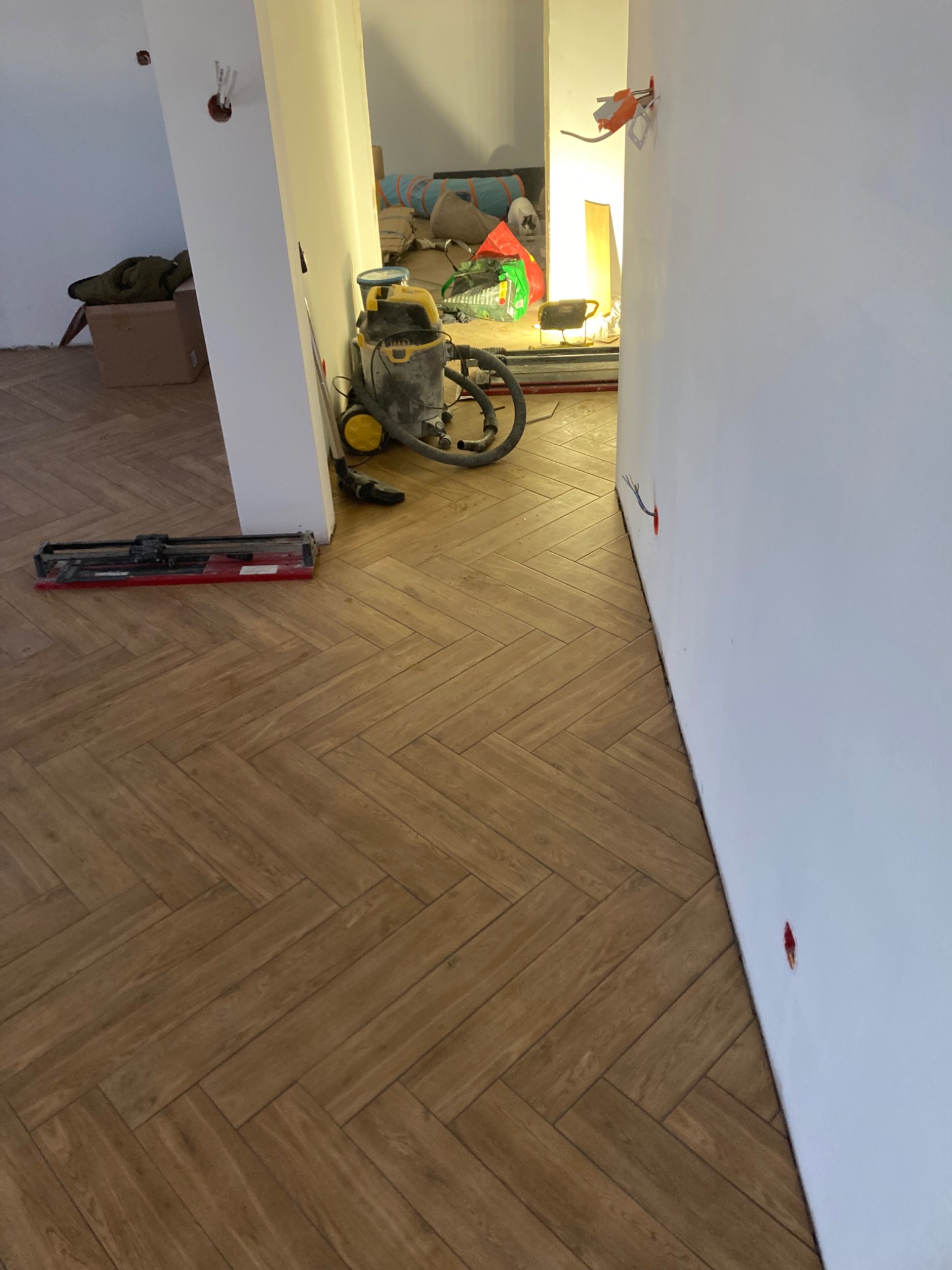 Ułożona podłoga z paneli w jodełkę, widoczny odkurzacz przemysłowy i przecinarka do płytek w trakcie prac wykończeniowych.