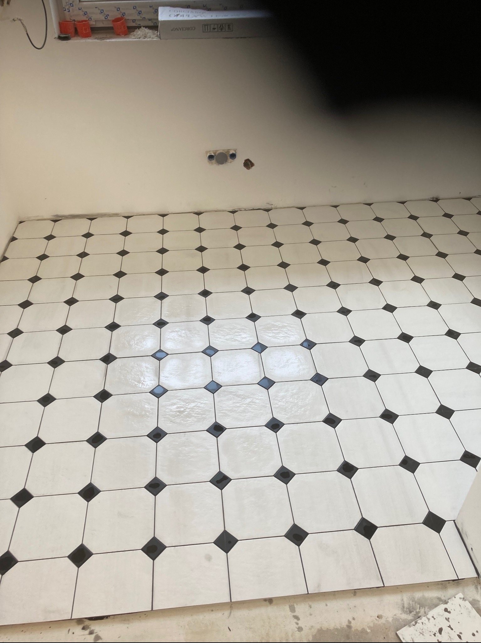 Ułożona podłoga z jasnych płytek z czarnymi akcentami w Olecku, widoczne puszki elektryczne w ścianie, etap prac wykończeniowych.