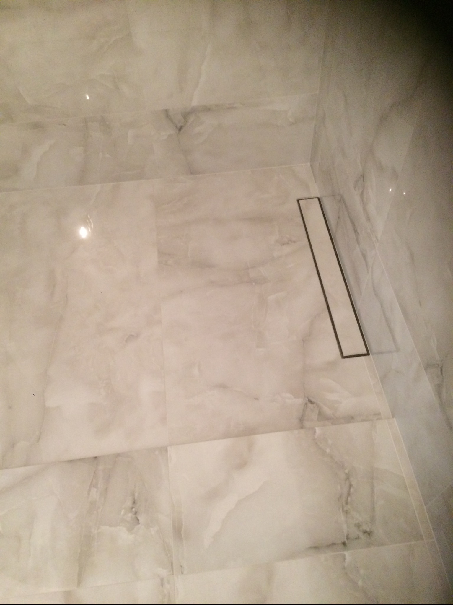 Wykończona łazienka z jasnymi, marmurkowymi płytkami i liniowym odpływem podłogowym z czarną ramką.