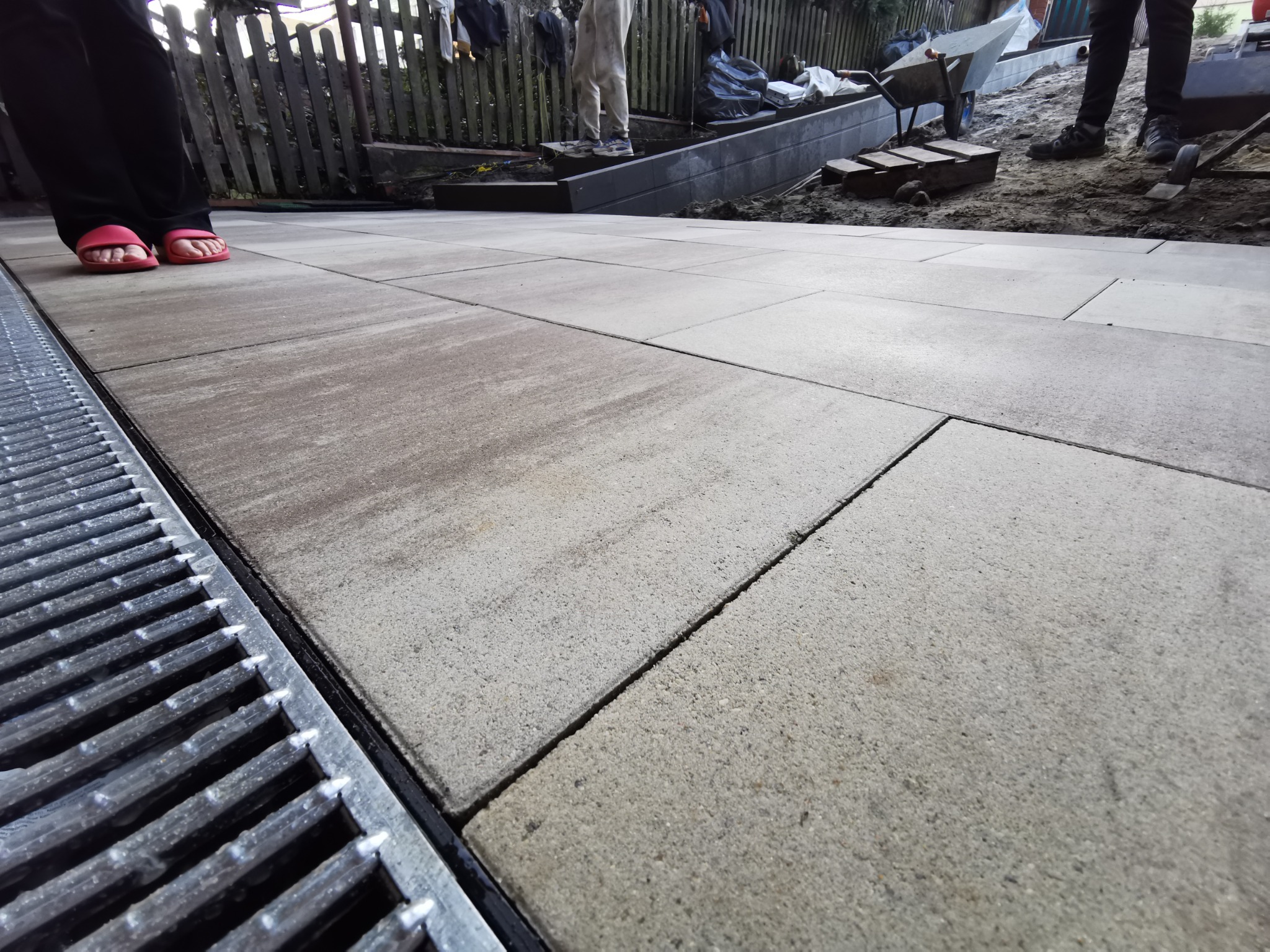 Ułożona kostka brukowa w Bieruniu z widocznym odpływem liniowym, fragmentem ogrodzenia i pracownikami w tle.