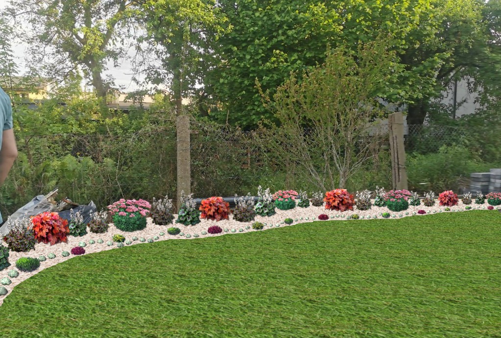 Aranżacja rabaty kwiatowej z kamykami na tle zieleni ogrodowej i drzew, z widocznym fragmentem osoby po lewej stronie kadru.