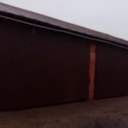 Duże, brązowe, przesuwne wrota garażowe z metalu, umieszczone w murowanym budynku z cegły, widziane z niskiej perspektywy przy pochmurnej pogodzie.