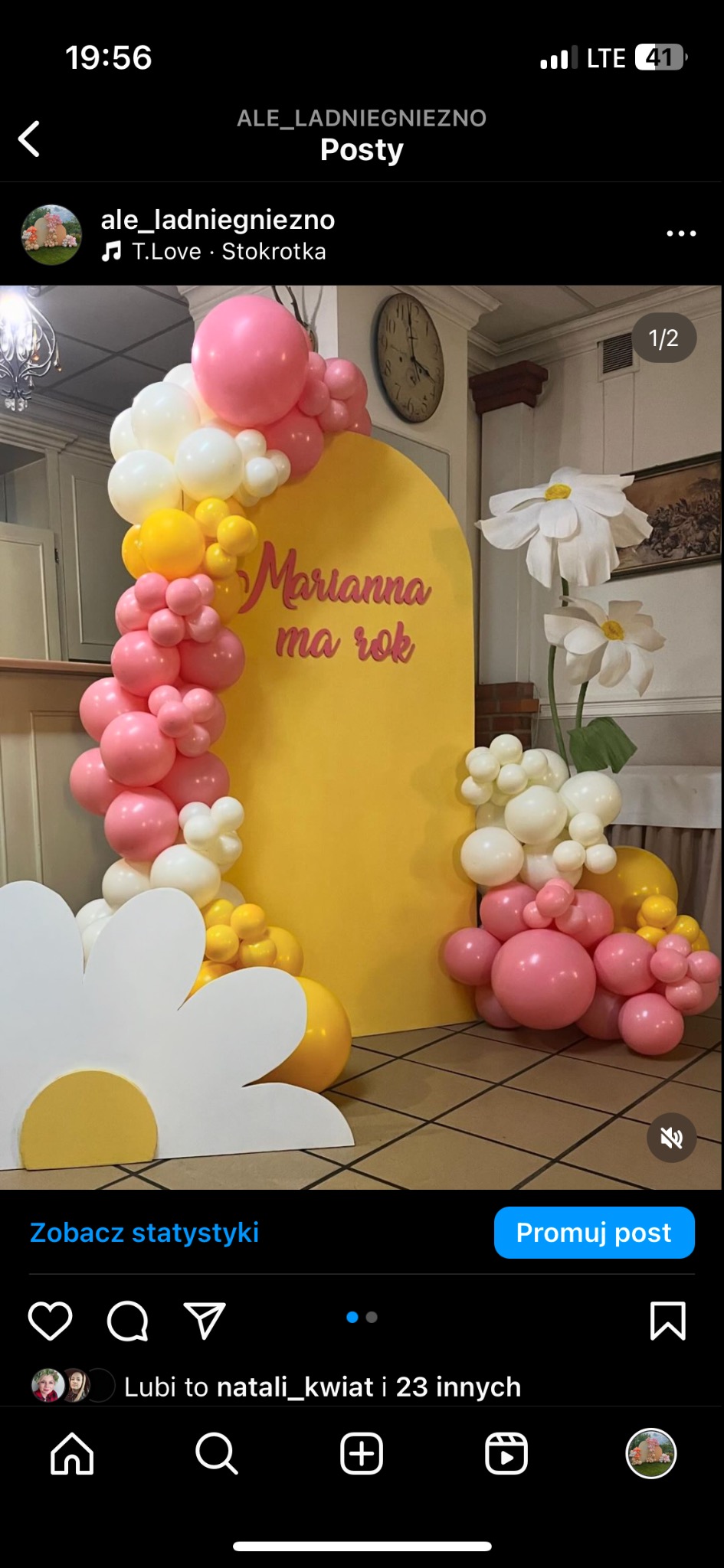 Dekoracja urodzinowa na roczek dziewczynki: żółty panel z napisem 'Marianna ma rok', girlanda z różowych, białych i żółtych balonów, duże papierowe kwiaty.