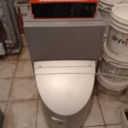 Kompaktowy piec kondensacyjny Viessmann z czerwonym panelem sterowania, widoczne rury instalacyjne i wiadra z materiałami budowlanymi w tle.