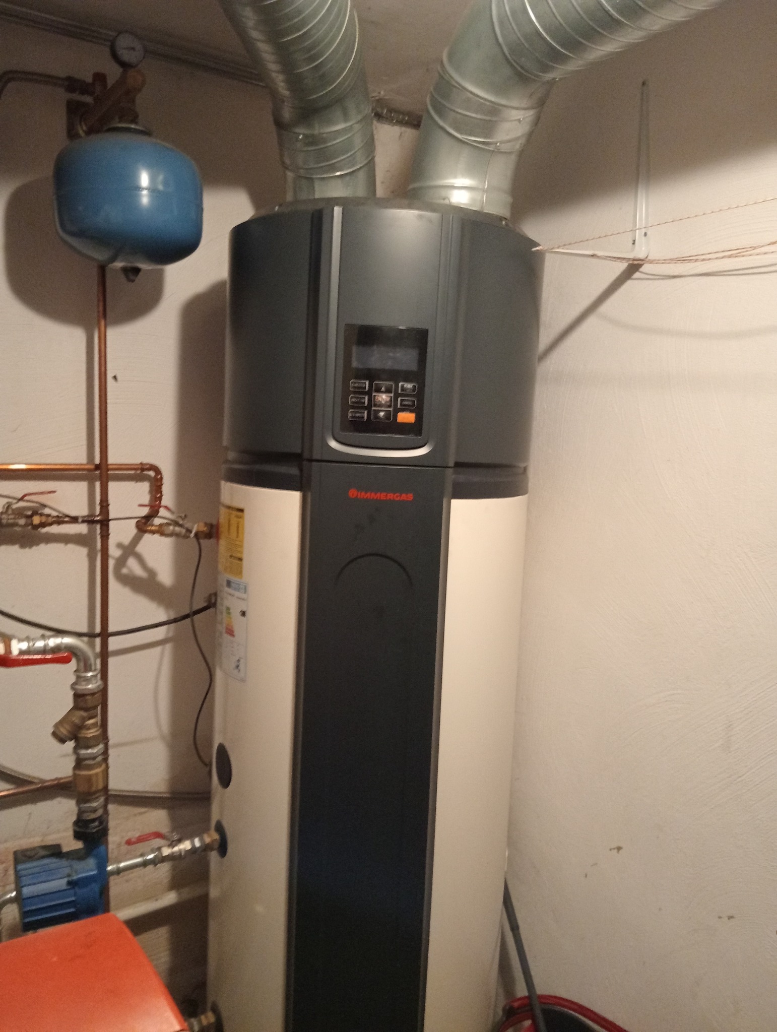 Stojący piec grzewczy marki Immergas z podłączonymi rurami, zbiornikiem wyrównawczym i pompą obiegową w pomieszczeniu technicznym.