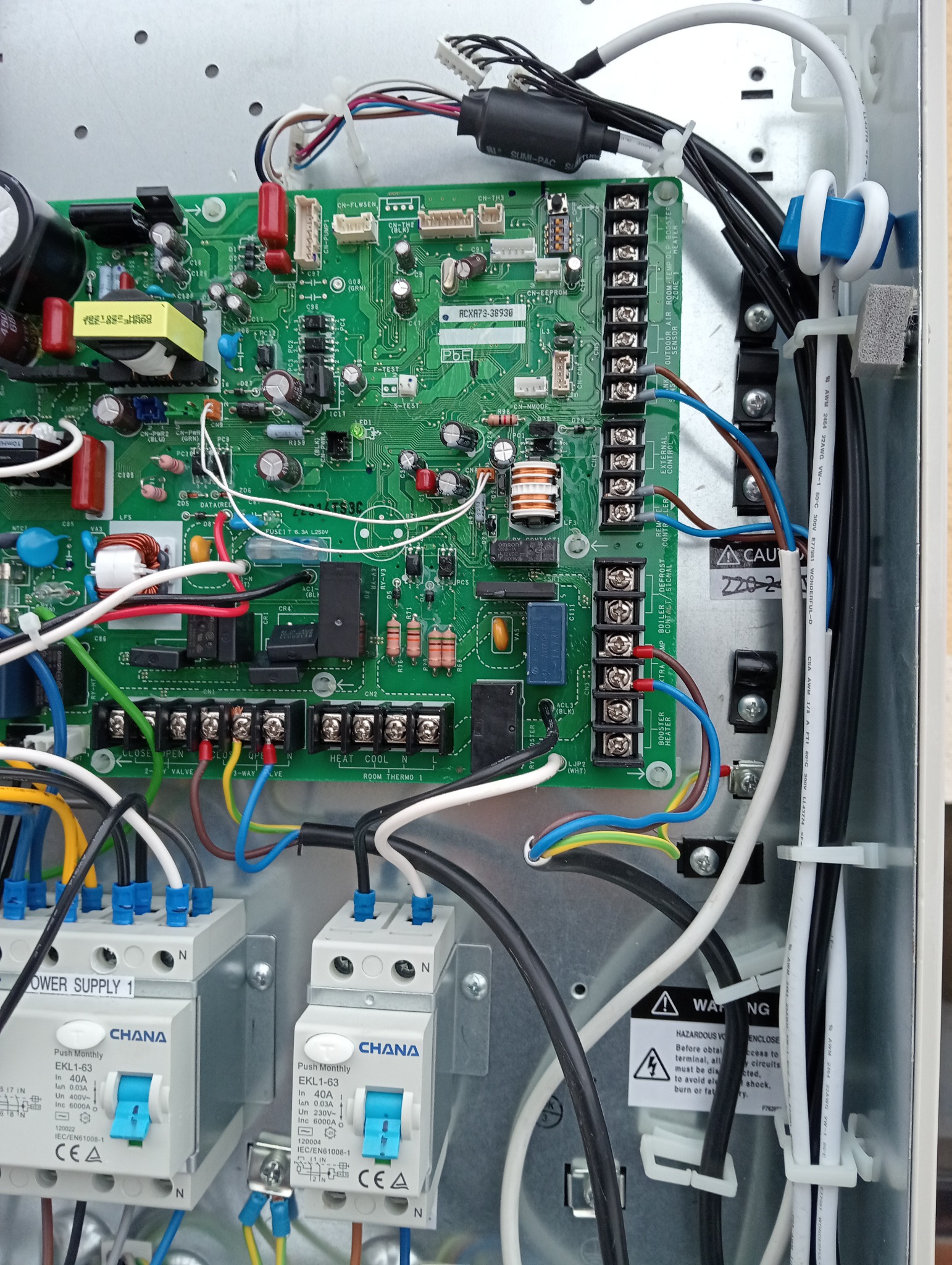 Otwarta obudowa sterownika z widoczną zieloną płytką drukowaną, licznymi przewodami, bezpiecznikami i przekaźnikami. Widoczne również dwa wyłączniki różnicowoprądowe marki Chana.