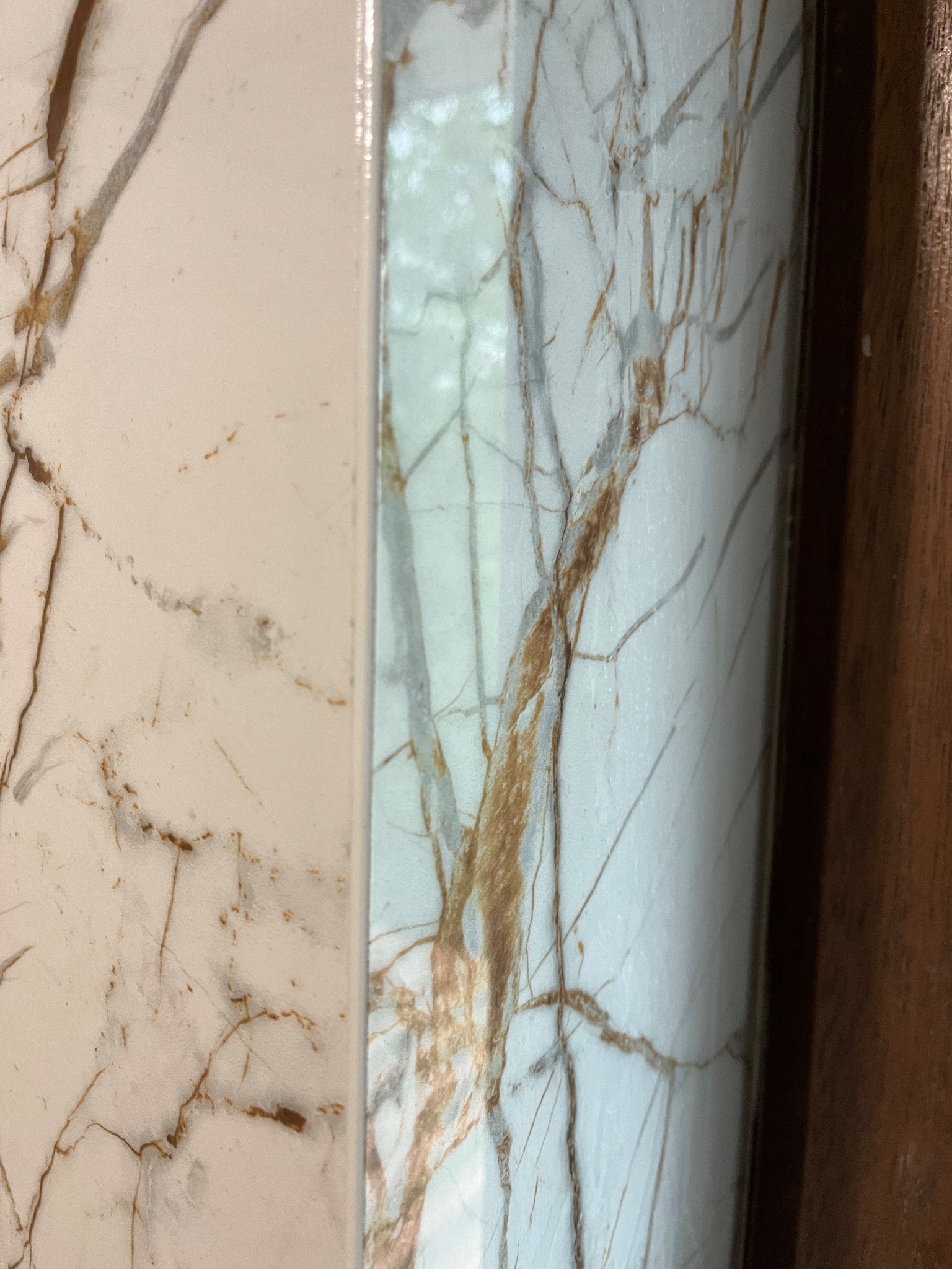 Fragment ściany wykończonej płytkami imitującymi marmur w odcieniach bieli i beżu z wyraźnym wzorem żyłkowania, przylegający do drewnianej listwy.