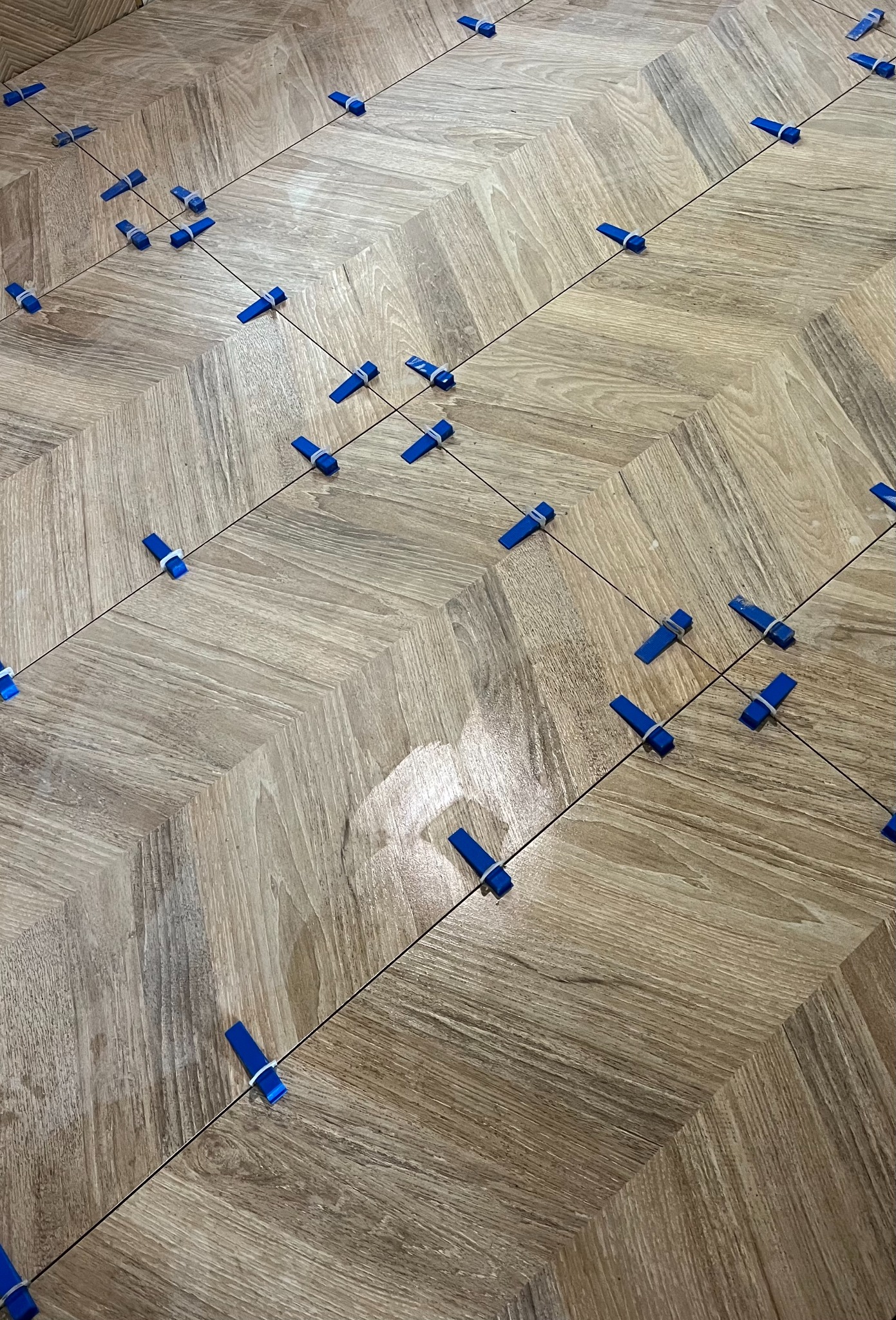 Ułożona w jodełkę podłoga z płytek imitujących drewno w trakcie montażu w Wudzynie, z użyciem niebieskich klipsów poziomujących.