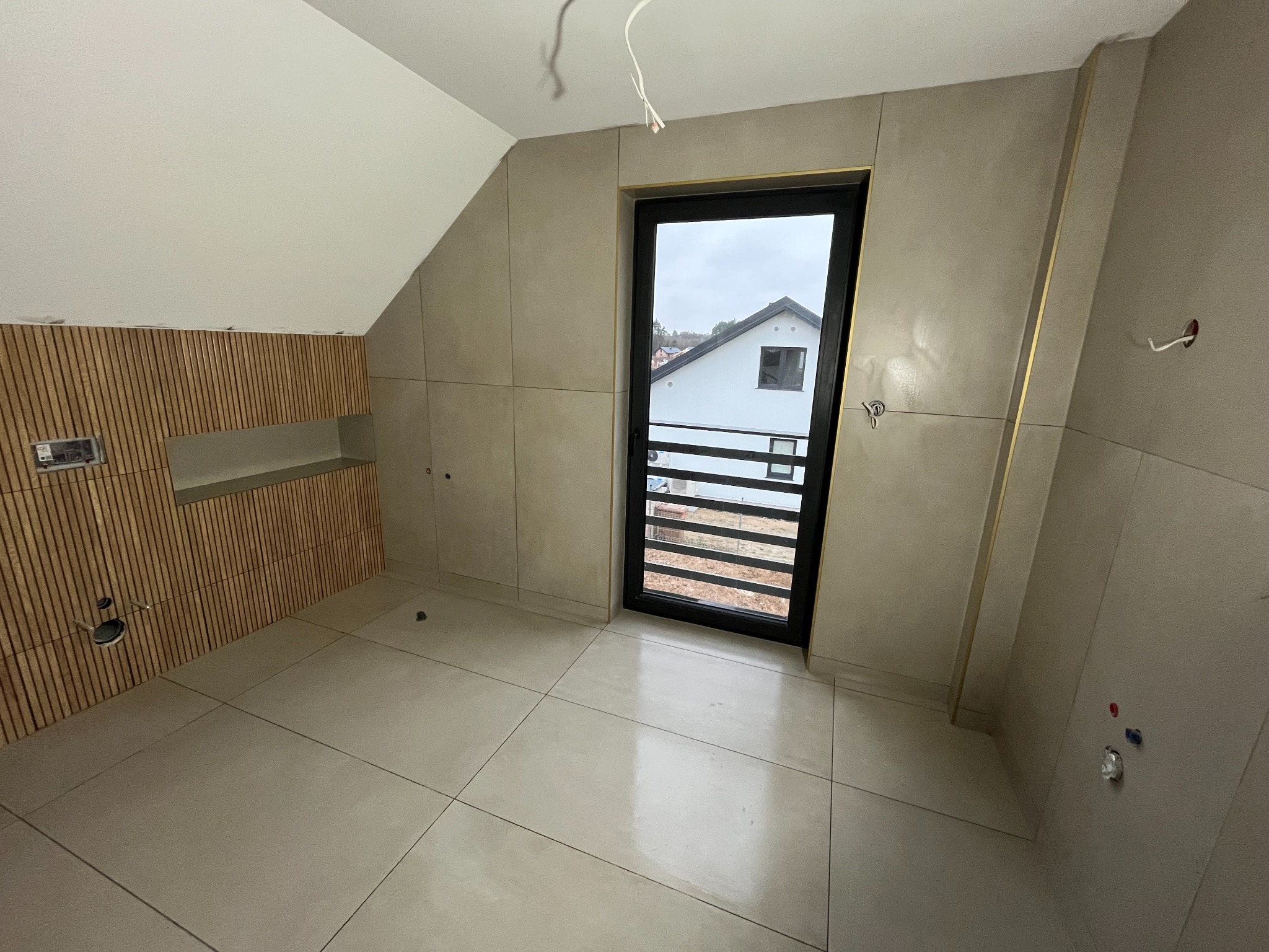 Łazienka w trakcie wykańczania: widoczne płytki podłogowe, okładzina ścienna z płytek imitujących beton z delikatnymi złotymi akcentami na krawędziach, drewniana okładzina z półką w skosie poddasza...