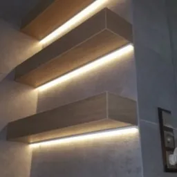 Trzy podświetlane półki z płytek imitujących drewno, zamontowane na szarej ścianie w łazience z widocznym fragmentem toalety.