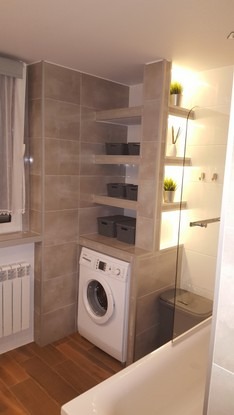Wykończona łazienka z pralką w zabudowie, półkami z szarymi pojemnikami i oświetleniem LED w pionowej wnęce.