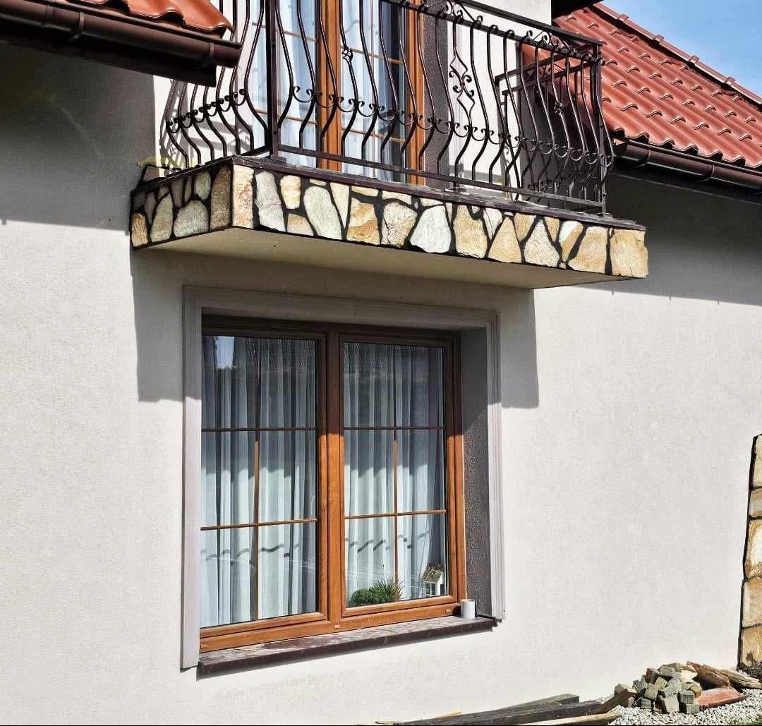 Elewacja domu z oknem w drewnianej ramie i balkonem z kutą balustradą, obłożonym kamieniem naturalnym.