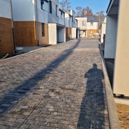 PRZEDSIĘBIORSTWO WIELOBRANŻOWE RADOSŁAW LICA - Nowa, ciemnoszara kostka brukowa ułożona na osiedlu domów jednorodzinnych w zabudowie szeregowej, widoczny cień osoby fotografującej.