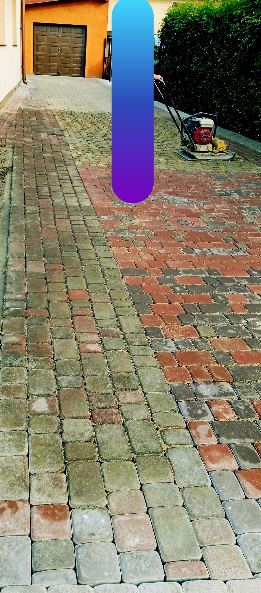 Układanie kostki brukowej na podjeździe, widoczna zagęszczarka w trakcie pracy, część powierzchni już wyrównana, a część jeszcze nie.