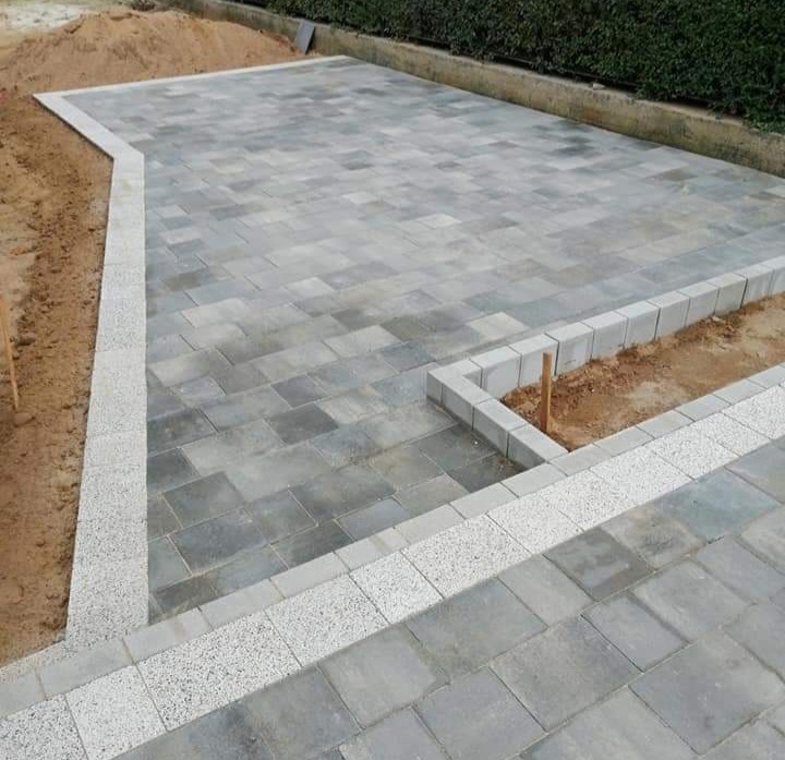 Ułożona szara kostka brukowa z obrzeżem z jasnej kostki na posesji, widoczne przygotowane miejsce na rabatę z obrzeżem z betonowych bloczków.