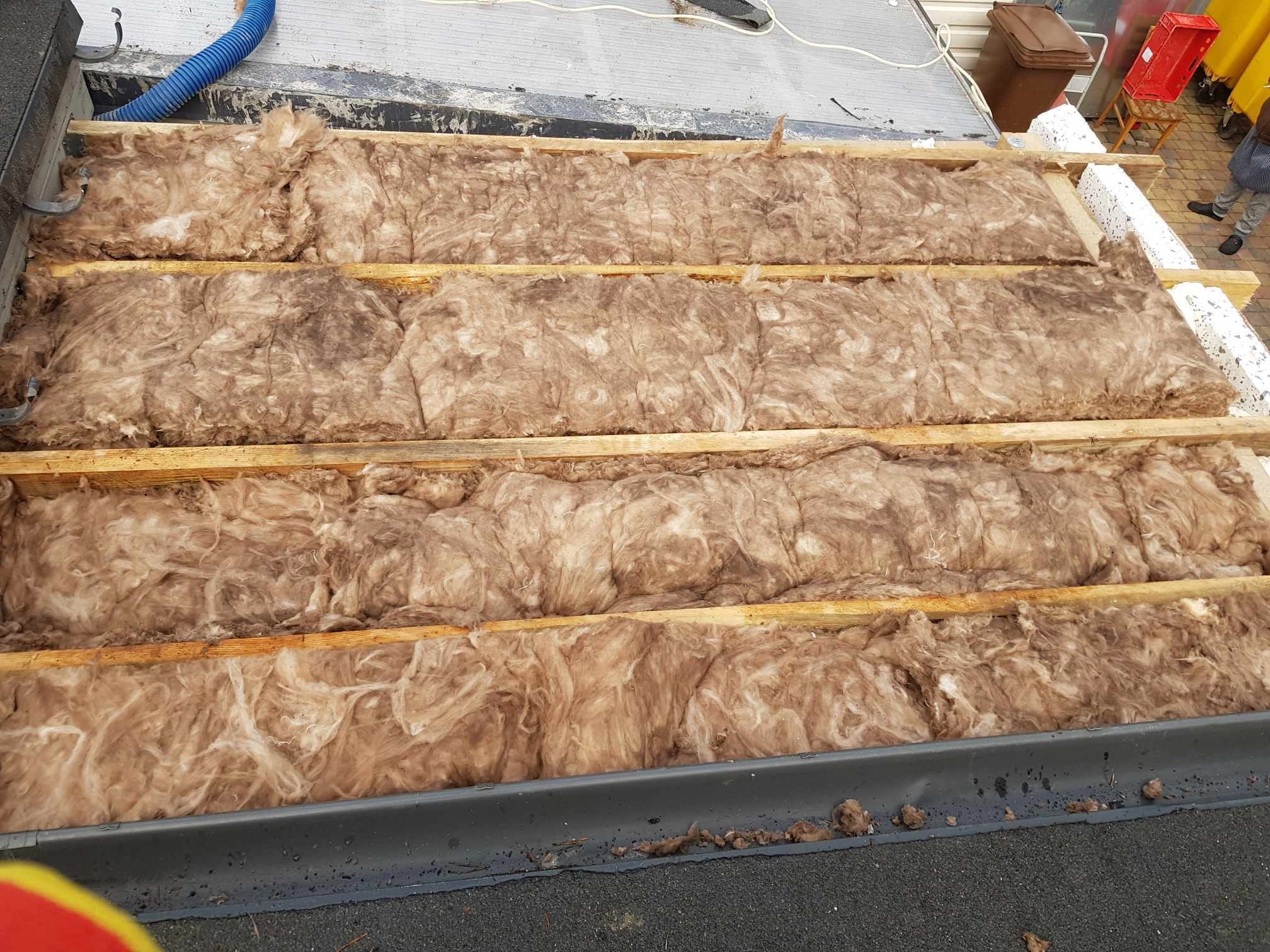 Ocieplenie dachu wełną mineralną pomiędzy drewnianymi legarami, widoczne elementy konstrukcji dachu i fragment otoczenia.