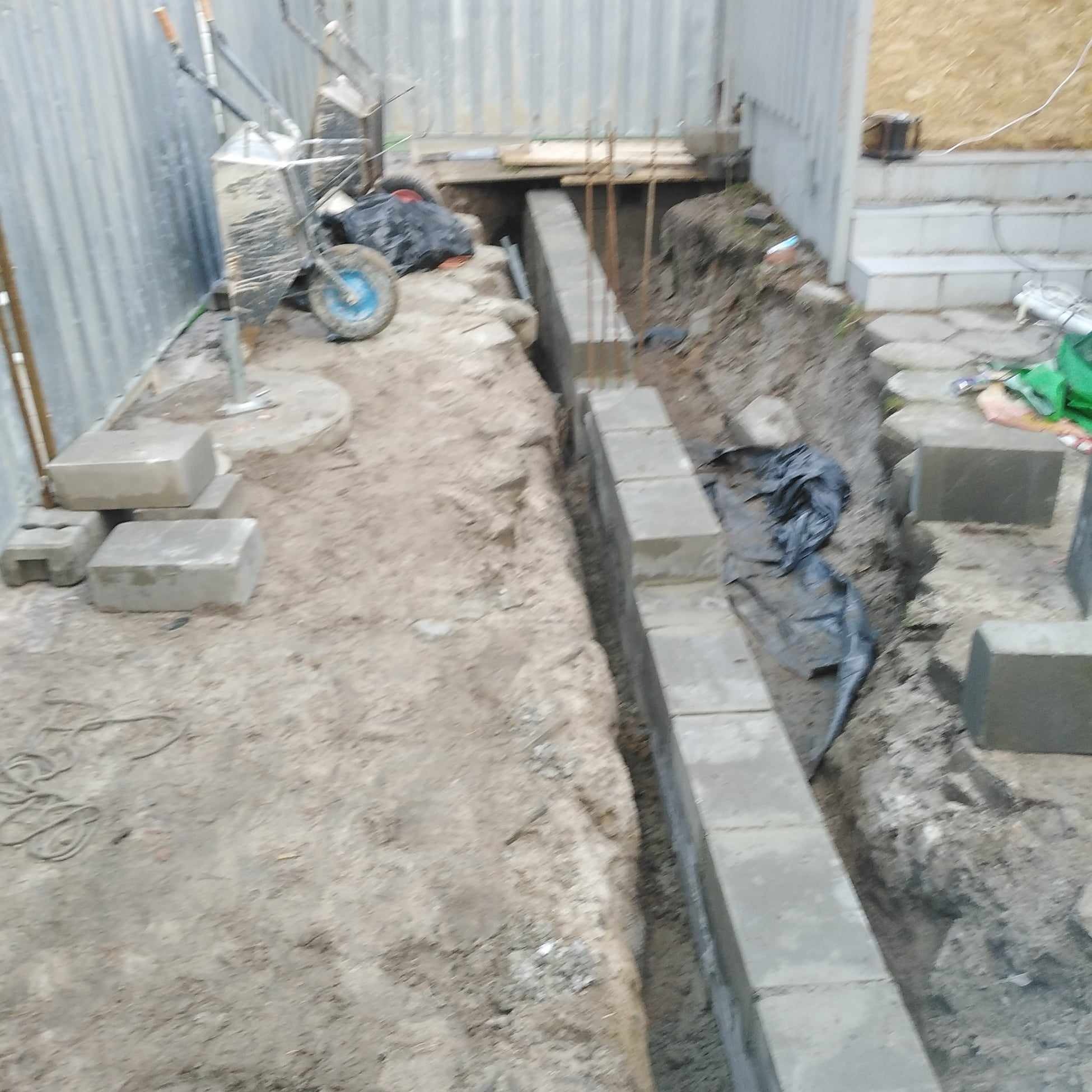 Fundament z betonowych bloczków w wykopie, widoczny wózek budowlany, etap budowy.