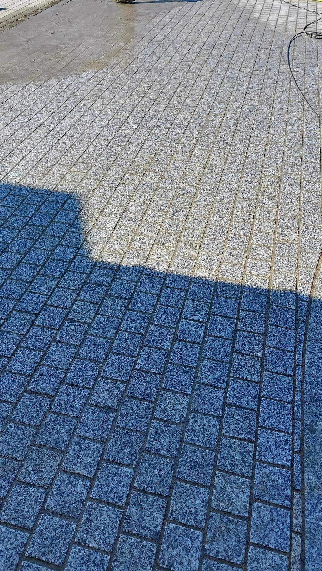 Ułożona kostka granitowa w dwóch odcieniach szarości, część mokra po czyszczeniu, widoczny cień osoby.