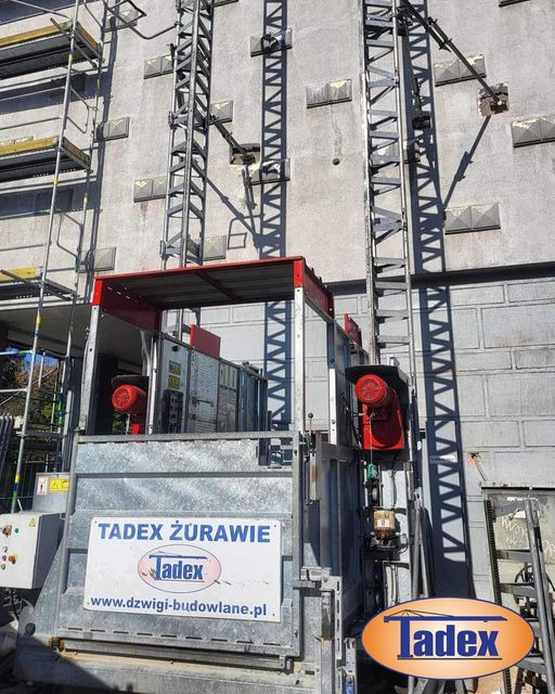 Winda budowlana z logo firmy Tadex Żurawie na tle elewacji budynku w Luboniu. Widoczne rusztowania i elementy konstrukcyjne.
