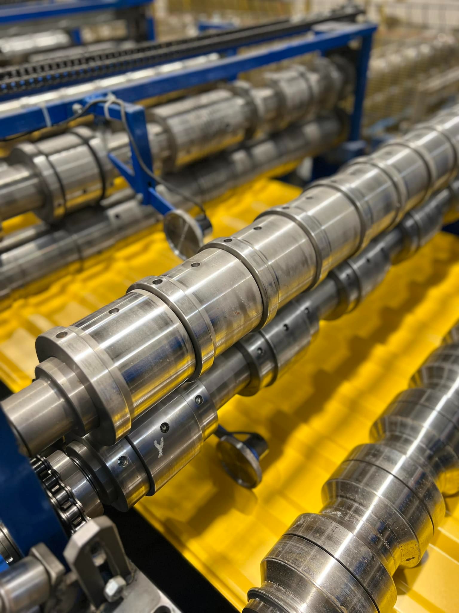 Szczegółowe ujęcie walców formujących blachę trapezową w maszynie produkcyjnej, widoczne ślady użytkowania i elementy łańcucha napędowego.