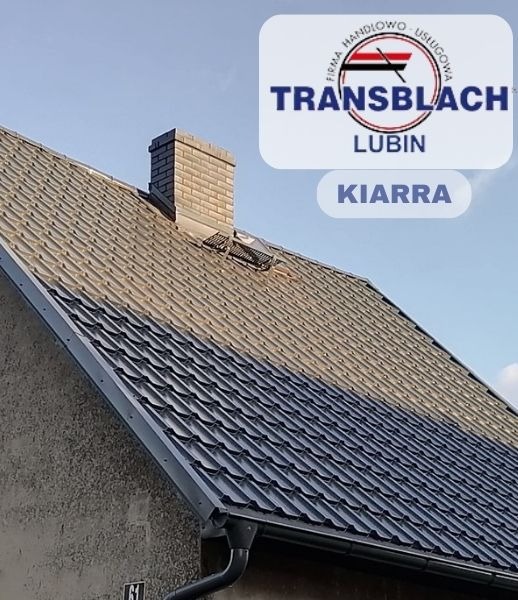 Nowy, ciemny dach z ceglanym kominem, częściowo pokryty szarym nalotem, z widoczną rynną i logiem firmy dekarskiej TRANSBLACH Lubin oraz nazwą modelu KIARRA.