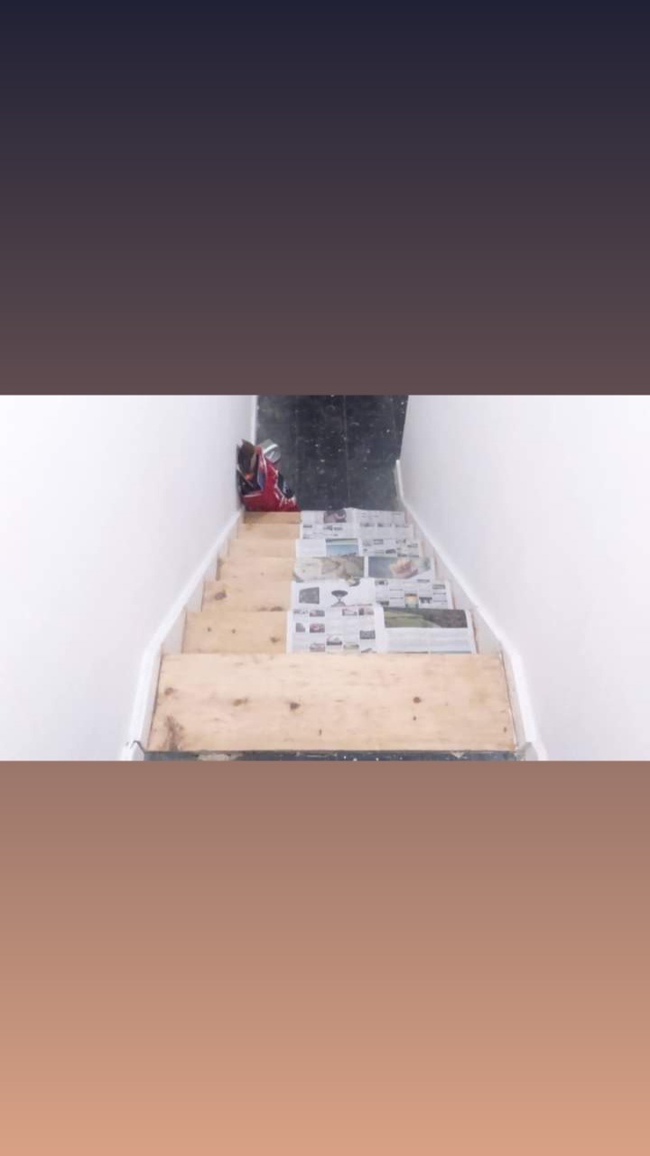 Klatka schodowa w trakcie remontu, zabezpieczona gazetami, z torbą narzędziową na górnym stopniu.