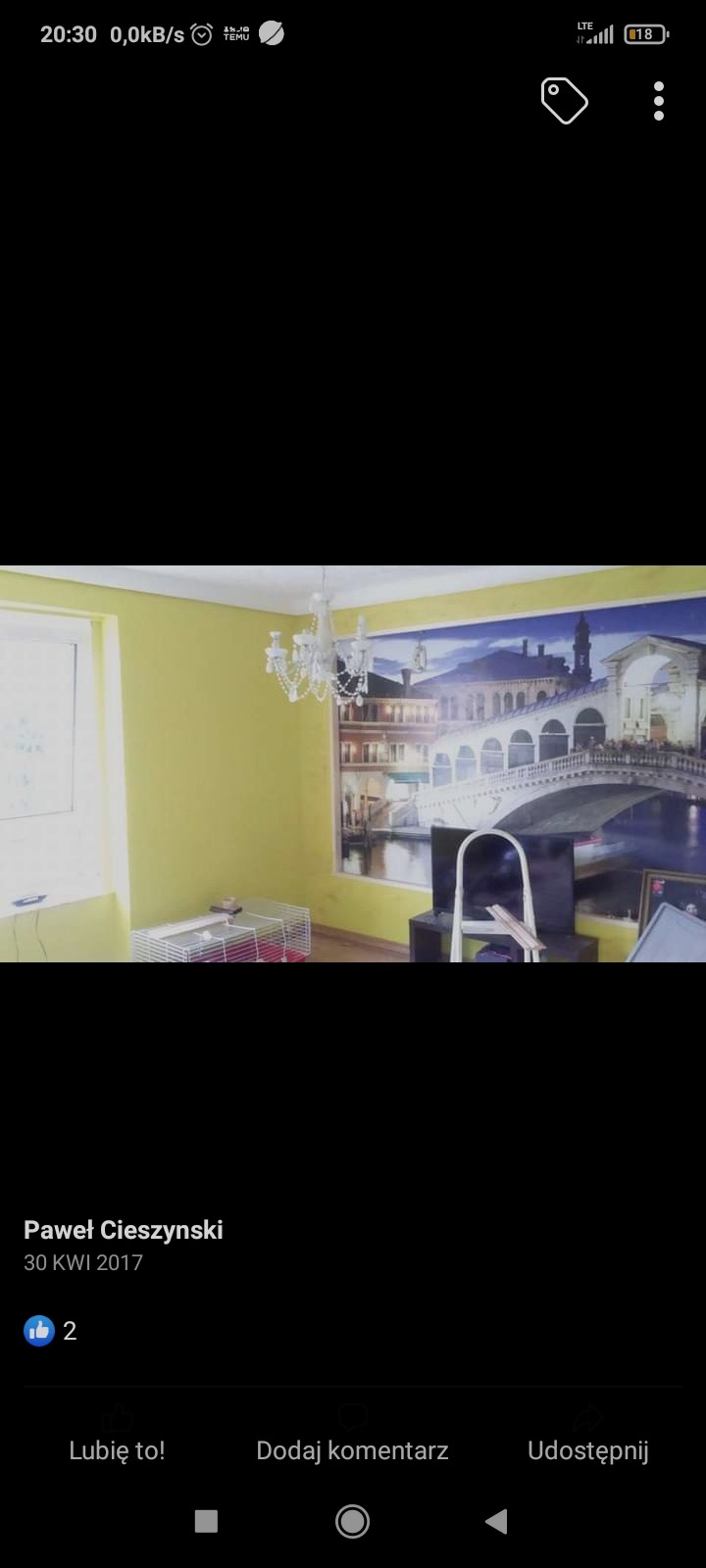 Pokój z żółtymi ścianami, ozdobiony fototapetą z motywem weneckim, widoczny biały żyrandol i klatka dla zwierząt, zdjęcie zrobione telefonem.