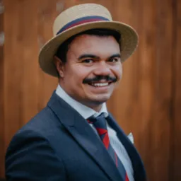 Uśmiechnięty mężczyzna w słomkowym kapeluszu, marynarce i krawacie w stylu retro, na tle drewnianej ściany. Portret w ciepłym oświetleniu.