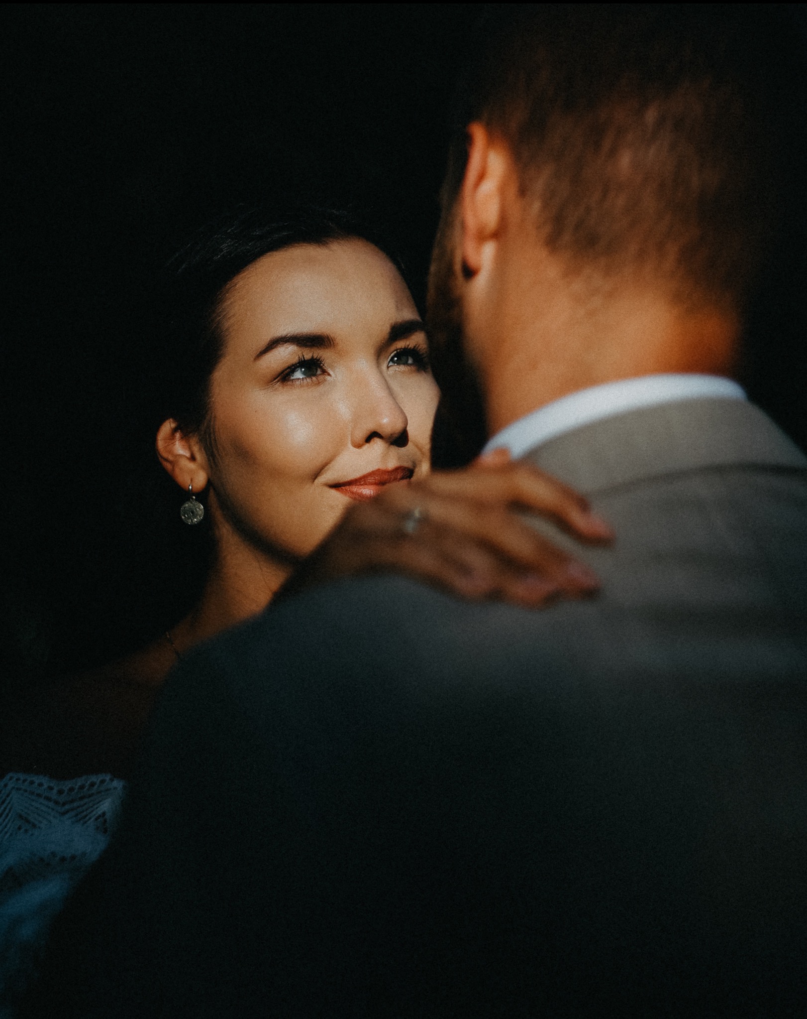 Zamyślona panna młoda wpatruje się w pana młodego podczas kameralnego tańca, oświetlona ciepłym blaskiem. Widoczny pierścionek zaręczynowy.