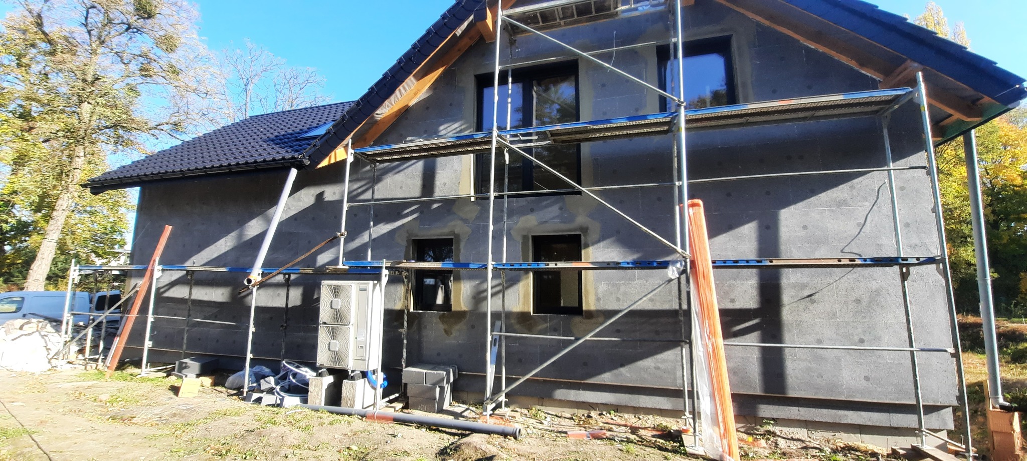 Dom jednorodzinny w trakcie ocieplania elewacji, widoczne rusztowania, styropianowe płyty na ścianach i jednostka zewnętrzna klimatyzacji