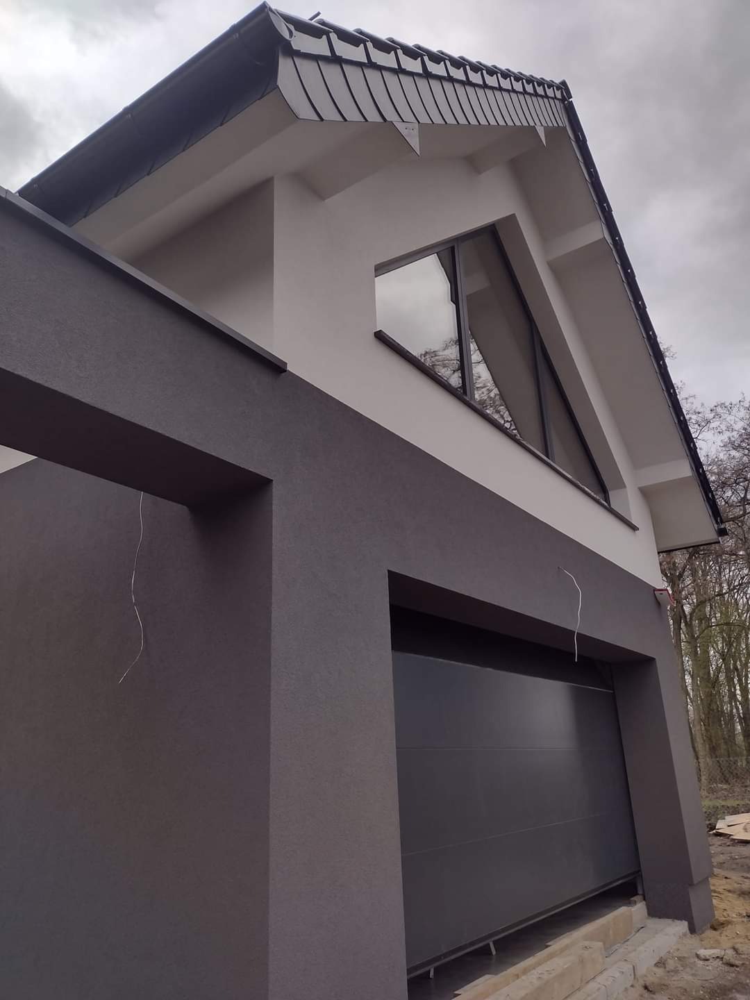 Dwukolorowa elewacja garażu z bramą segmentową i trójkątnym oknem, widok z dołu na tle pochmurnego nieba.