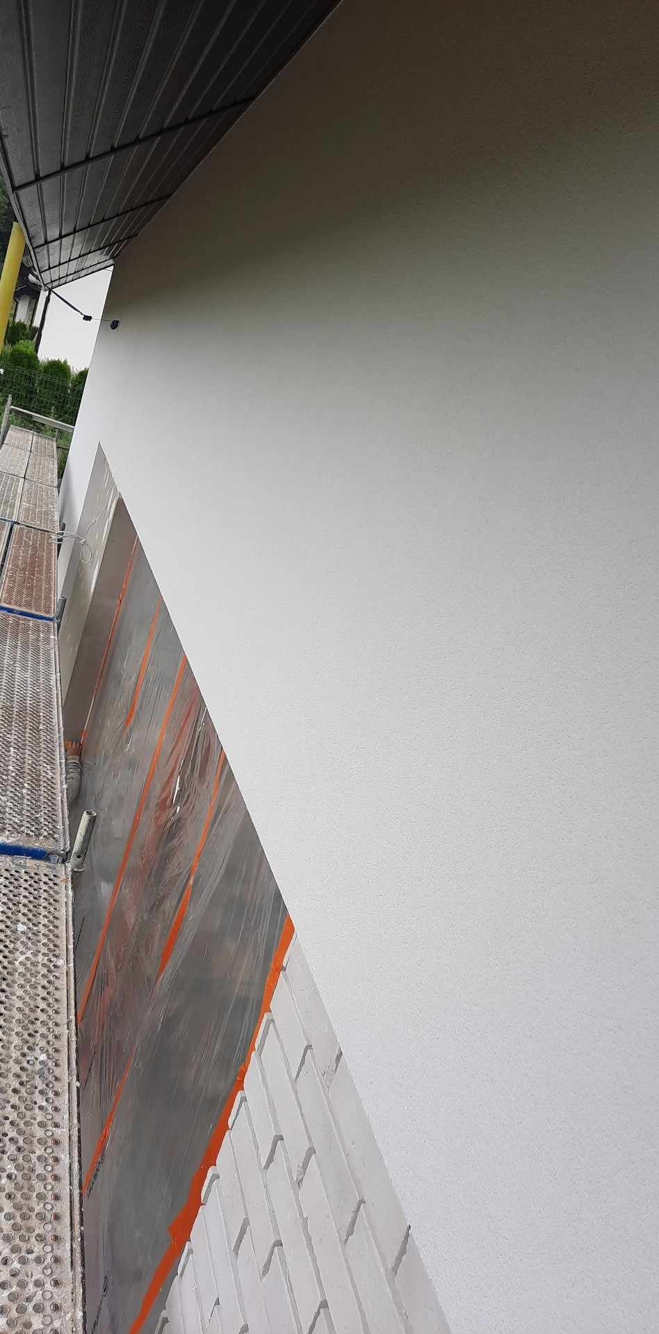 Świeżo pomalowana, biała elewacja domu jednorodzinnego, zabezpieczona folią okienna, widoczny fragment rusztowania.